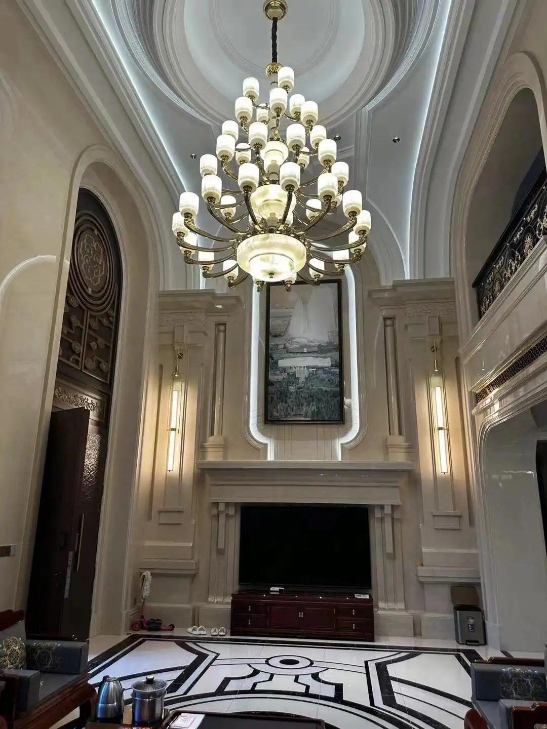Decoratief marmeren vloermedaillon met een zwart-wit geometrisch, radiaal zonnestraal- of kompasroosmotief, gesneden met een waterstraalsnijder; zwart marmer met opvallende witte aders, een gedetailleerd caleidoscopisch ontwerp onder een cassetteplafond met een kristallen kroonluchter met meerdere rijen in de luxueuze lobby met dubbele plafondhoogte