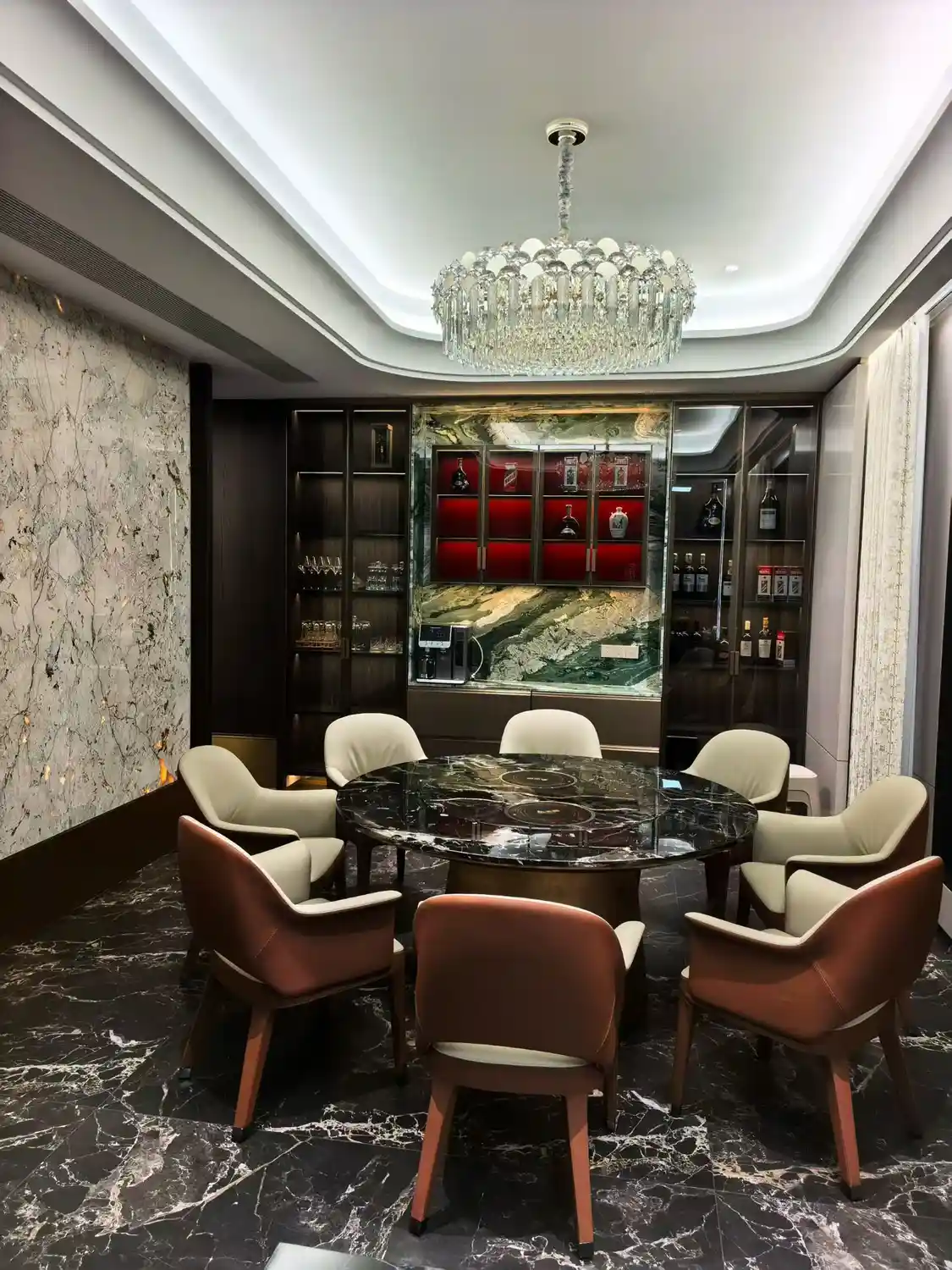Luxe eetkamer met een opvallende wand van exotisch groen marmer (Verde Alpi of Guatemala Green) met indrukwekkende witte aders, een gepolijste zwarte marmeren vloer met opvallende witte aderpatronen (Nero Marquina), een wandpaneel van grijsgroen marmer in book-matched uitvoering en een kristallen kroonluchter in een moderne, luxe woning