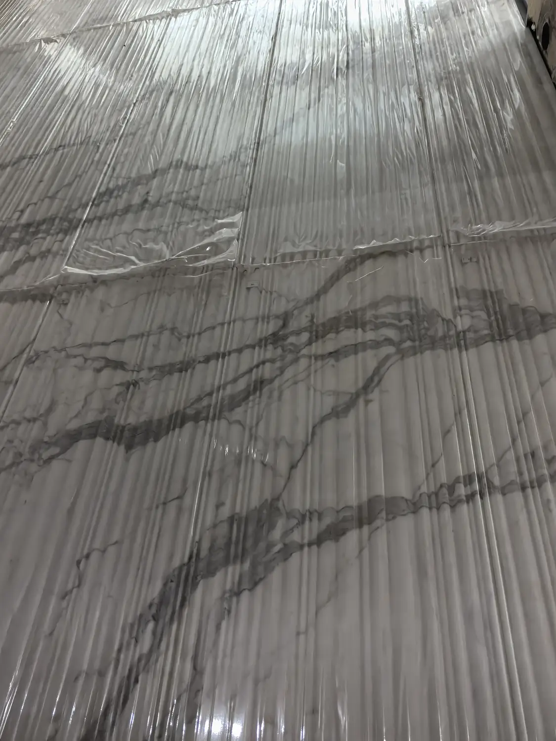 Wandbekleding van wit en grijs marmer met zichtbare aders en opvallende horizontale donkergrijze aderstrepen, grootformaat gepolijste marmeren platen met een geribbelde of gegroefde verticale structuur, moderne, luxueuze accentwand met marmer in Calacatta- of Statuario-stijl, gelegd in book-matched-patroon