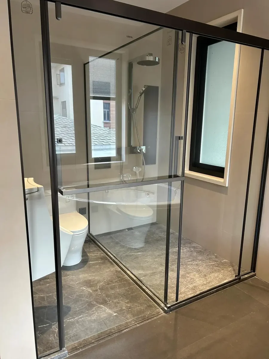 Polished grey veined marble flooring installed in a contemporary minimalist luxury bathroom featuring subtle beige and cream veining throughout, complemented by glass shower enclosure with chrome fittings, white wall-mounted toilet, and modern chrome fixtures creating an elegant spa aesthetic, premium quality marble tile installation for upscale residential bathroom floors, combining neutral grey marble's versatile character with modern minimalist bathroom design for sophisticated master bath and guest bathroom renovations